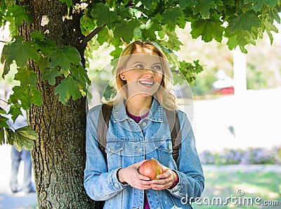 Girl student with backpack hold apple while stand near tree. Healthy snack. Students life concept. Take minute to relax Stock Photo