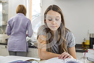 Girl studying at table with mother standing in background Stock Photo