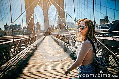 Girl in sunglasses strolls along the Brooklyn Bridge in New York City at sunset Stock Photo