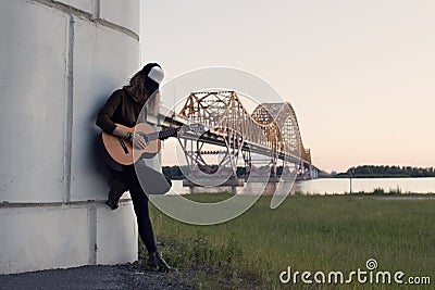 Girl with a guitar standing at the foot of the bridge over the r Stock Photo