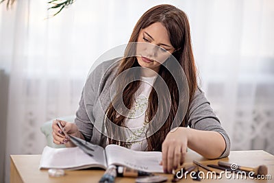 A girl in a sweater and t-shirt sits at a table and flips through a magazine Stock Photo