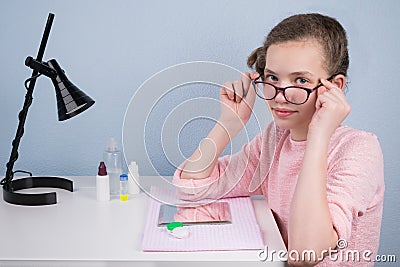 The girl takes off her glasses, sitting at the table, in order to wear the lens for correcting the sight Stock Photo