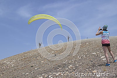 A girl takes a picture of people flying on a parachute. Edge of Editorial Stock Photo