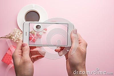 Girl takes pictures on a phone on a pink background of coffee and macaroons, for an instagram Stock Photo