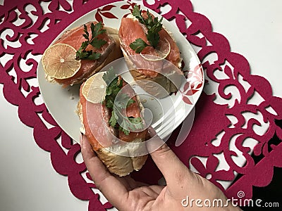 The girl takes the sandwich from the plate. Sandwiches with salmon, decorated with greens and lemon. Sandwiches on a plate, standi Stock Photo