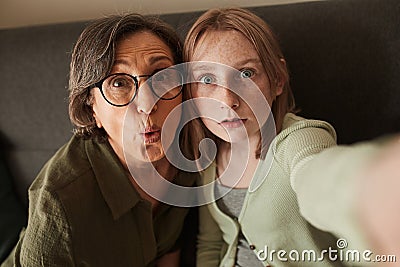 Girl taking self portrait with her funny granny while spending time at the sofa Stock Photo