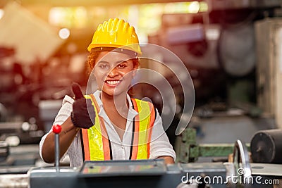 Girl teen worker with safety helmet show thumb up working as labor in industry factory with steel machine Stock Photo