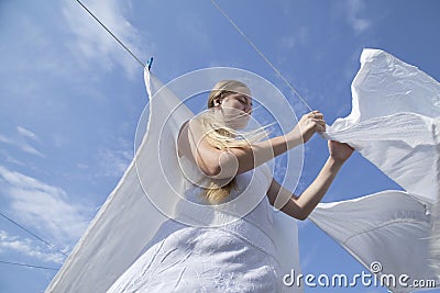 Girl teenager is hung up white sheets on clothesline fixing them with clothespins Stock Photo