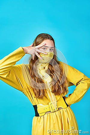 Girl teenager in yellow mask on her face makes gesture with her fingers. blue background Stock Photo