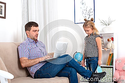 Dad is sitting on the couch with laptop, he is very busy. The daughter is ignored by the father, she is upset Stock Photo