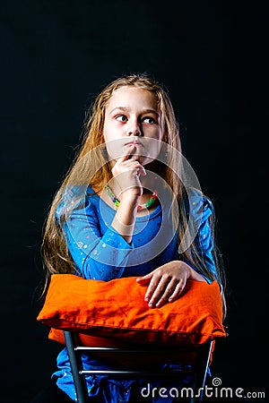 Girl thinks sitting on a chair on a black background Stock Photo