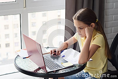 Girl thoughtfully doing homework, sitting at a table by the window Stock Photo