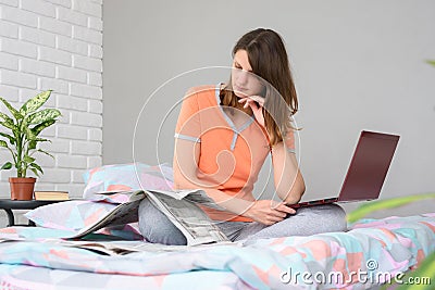 Girl thoughtfully reads newspaper ads while sitting on bed at home Stock Photo