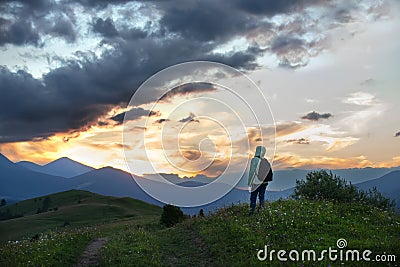A girl tourist admires the sunset in the mountains. Silhouettes of mountains against the background of the sunset sky Stock Photo