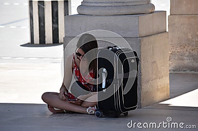 girl tourist with a large suitcase sits on the Palais Royal in Paris looks at the phone editorial Paris summer 2019 Editorial Stock Photo