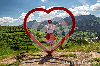 Girl in traditional costume posing with red wooden heart in village Terchova at Slovakia Editorial Stock Photo