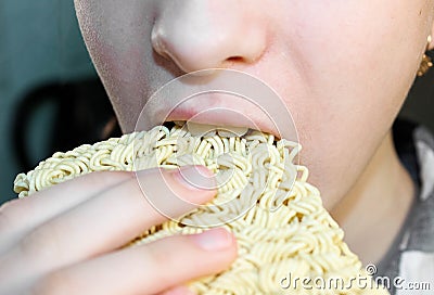 The girl tries to bite off a bar of dry Chinese instant noodles Stock Photo