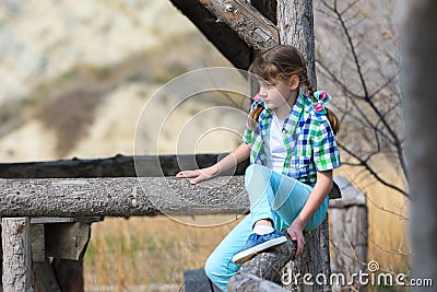 A girl tries to sit on a fence made of a thick wooden frame Stock Photo