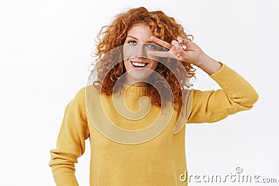 Girl trying stay positive any situation. Attractive happy redhead curly woman in yellow sweater showing peace, victory Stock Photo