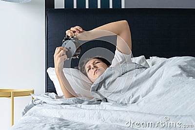 The girl turns off the annoying alarm clock to continue sleeping. Get some more sleep. It a hard morning. Time to wake up Stock Photo