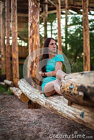 Girl in turquoise short dress sitting on a tree log Stock Photo