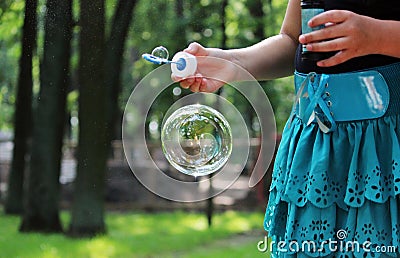 Girl in turquoise skirt let one large bubble in the summer park. Stock Photo