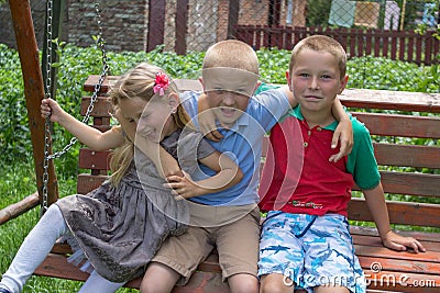 Girl with two brothers,meeting of classmates` children on the bench embrace Stock Photo