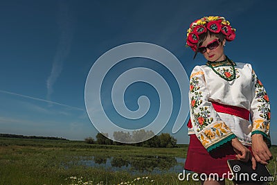 A girl in Ukrainian embroidery with a wreath on her head by the lake in a meadow among the flowers Editorial Stock Photo