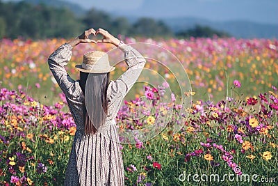The girl uses her hand to make a heart symbol to show the love and friendship to her lover on a beautiful cosmos flower field in Stock Photo