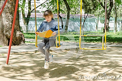 Girl on a walk reading a book swinging on a swing at the playground Stock Photo