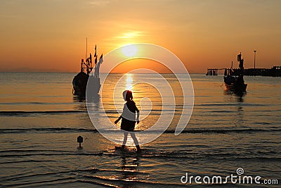 The girl walked on the beach with a fishing boat and sunset. Stock Photo