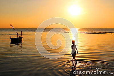 The girl walked on the beach with a fishing boat and sunset. Stock Photo