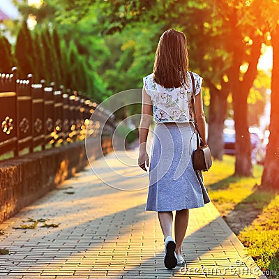 Girl walking away through green alley at the sunset Stock Photo