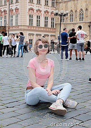 The girl in a pink undershirt and in dark glasses sits on stone blocks at Old Town Square in Prague. Editorial Stock Photo