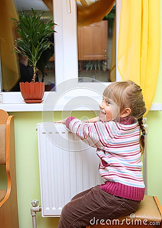 Girl warm one's hands near radiator. Stock Photo