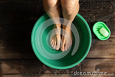 Girl washes her feet in a green bowl on the wooden floor of the house, foot care Stock Photo