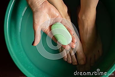 girl washes her feet in a green bowl on the wooden floor of the house, foot care Stock Photo