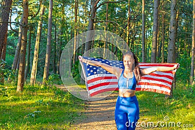 Girl waving American flag.Attractive patriotic American girl wrapped usa flag at summer forest Stock Photo