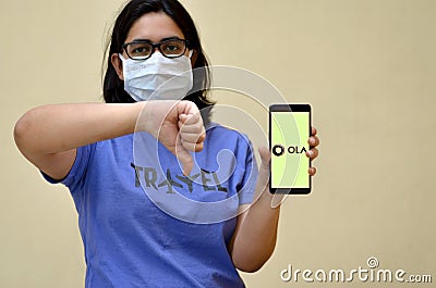 Girl wearing mask showing Ola app on her mobile phone screen showing thumbs down against yellow background.Its an aggregator Editorial Stock Photo