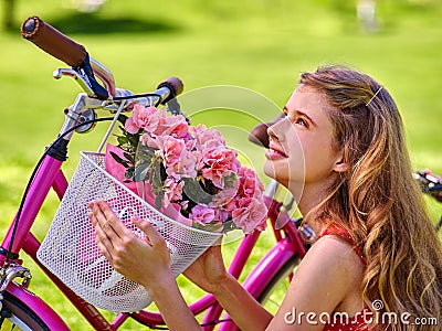 Girl wearing sundress rides bicycle with flowers basket. Stock Photo