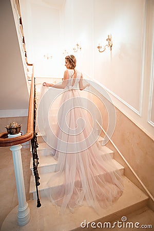 A girl in a wedding dress is walking up the stairs. beige dress. Beautiful lady in luxurious ballroom dress walking up the stairs Stock Photo