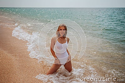 A girl in a white bodysuit is kneeling in sea water on the shore Stock Photo