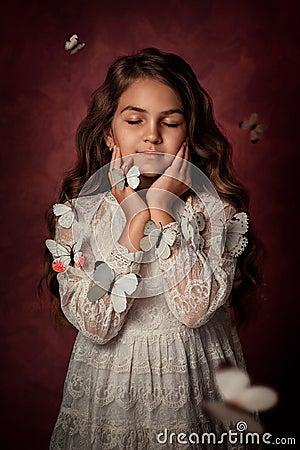 A girl in a white dress closed her eyes, her hands near her face. White butterflies fly around the girl. Stock Photo