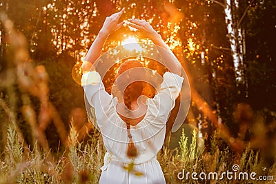 The girl in a white dress looks at the sunset in the forest and relaxes. Woman with braid hairstyle meditation Stock Photo