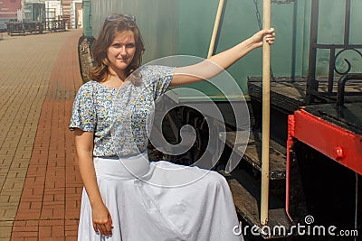 Girl in a white dress sits on the train. Woman is preparing to sit in the car. Farewell before sending the train on platform. Stock Photo