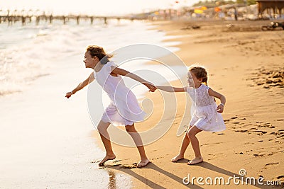 Girl in white dresses playing on beach. older sister pulls younger into water Stock Photo