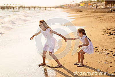 Girl in white dresses playing on beach. older sister pulls younger into water Stock Photo
