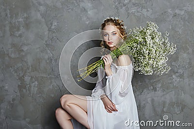 Girl white light dress and curly hair, portrait of woman with flowers at home near the window, purity and innocence. Curly blonde Stock Photo