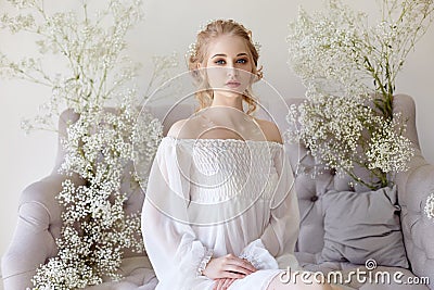 Girl white light dress and curly hair, portrait of woman with flowers at home near the window, purity and innocence. Curly blonde Stock Photo