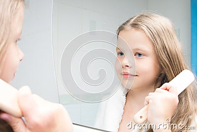 A girl in a white robe, in the bathroom, combs her hair and looks in the mirror Stock Photo